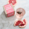 Box of 10 pink grapefruit cold brew tea temples next to a prepared glass of cold brew tea 