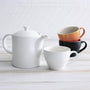 Cotton Le Creuset teapot next to trio of le creuset mugs in cotton, satin black, and volcanic